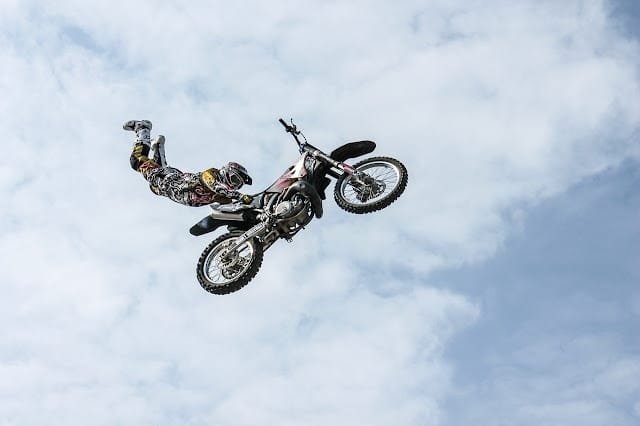 A person performing a stunt, flying through the air while doing a handstand on a motorcycle