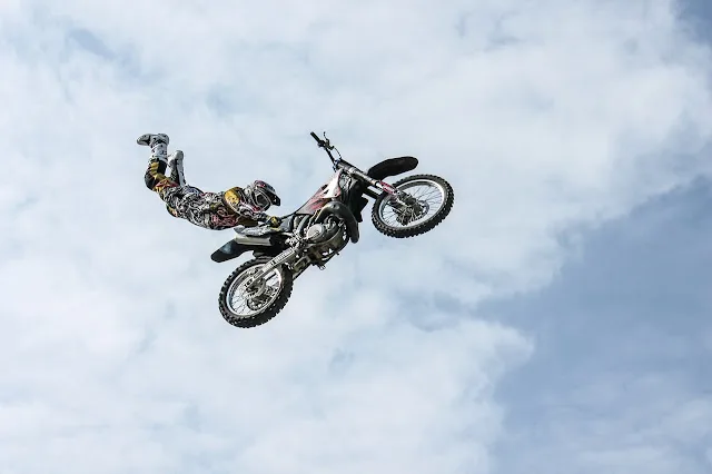 A person performing a stunt, flying through the air while doing a handstand on a motorcycle