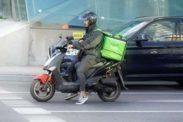The food delivery driver is riding a motorcycle.