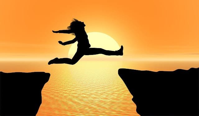 A person is jumping between cliffs against the backdrop of a sunset.