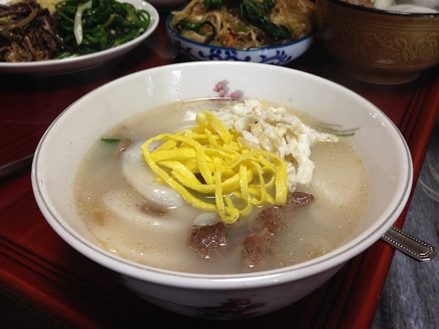 A close-up of traditional Korean Tteokguk (rice cake soup) topped with shredded yellow egg garnish and seasoned beef pieces, ready to be served for Seollal (Lunar New Year).